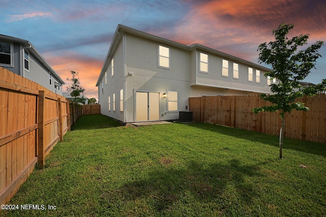 back house at dusk with a yard and central AC