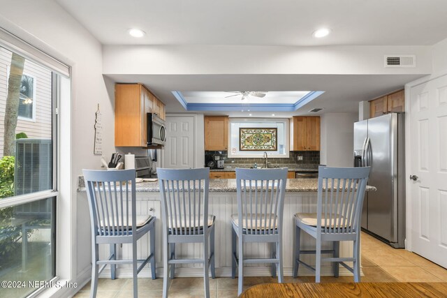 kitchen featuring stone counters, appliances with stainless steel finishes, kitchen peninsula, a kitchen bar, and tasteful backsplash