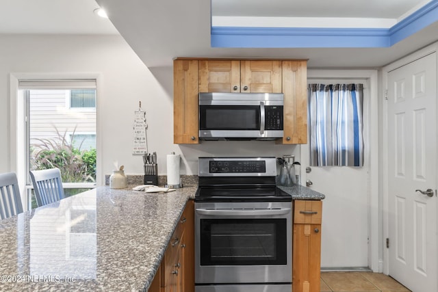 kitchen with dark stone countertops, light tile patterned floors, and stainless steel appliances