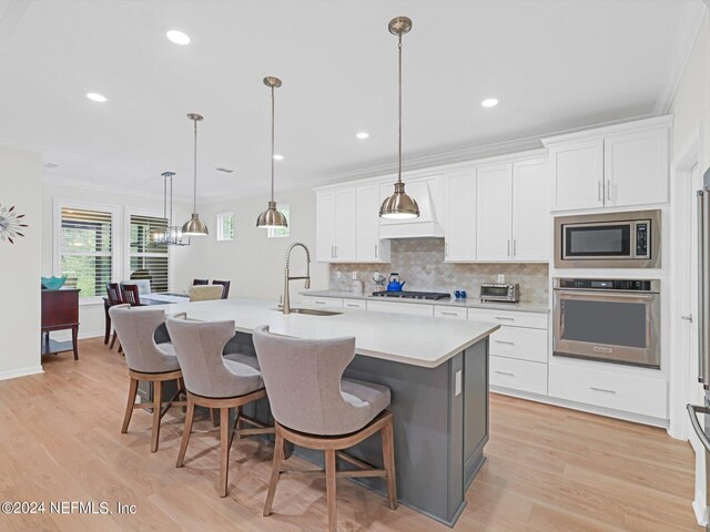 kitchen with light hardwood / wood-style flooring, stainless steel appliances, white cabinets, and a kitchen island with sink