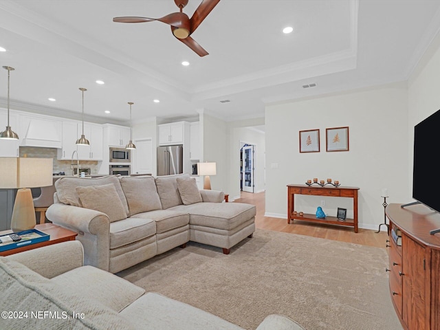 living area with light wood-style floors, a raised ceiling, and crown molding