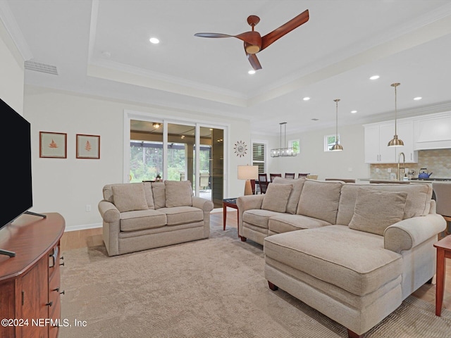 living area featuring a ceiling fan, a tray ceiling, crown molding, and light wood finished floors