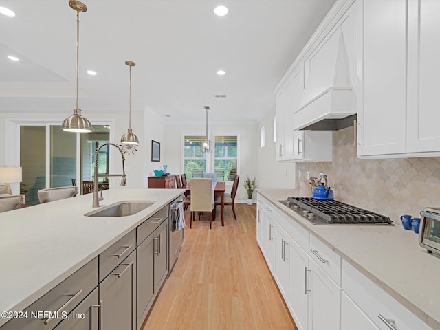 kitchen with light wood finished floors, custom range hood, backsplash, appliances with stainless steel finishes, and a sink