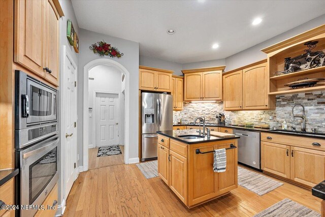 kitchen with a kitchen island with sink, stainless steel appliances, sink, and light hardwood / wood-style floors