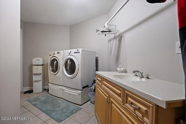 laundry area with cabinets, a textured ceiling, light tile patterned floors, washer and dryer, and sink