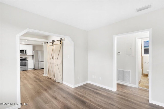 spare room with a barn door, electric panel, and light hardwood / wood-style floors