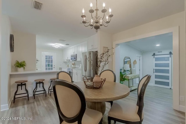 dining area featuring a barn door, light hardwood / wood-style flooring, and a chandelier