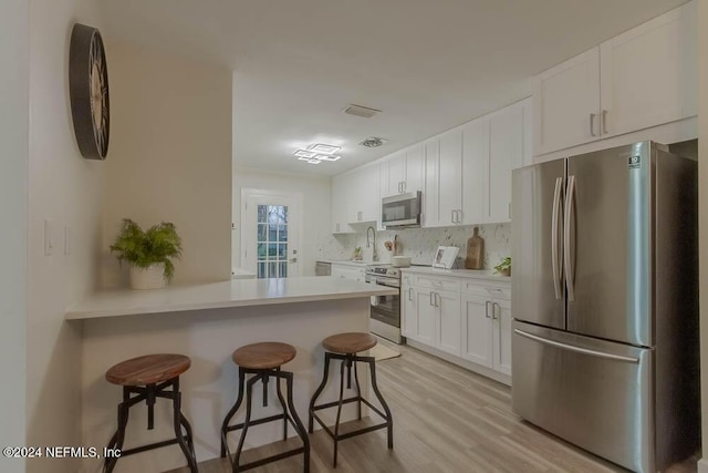 kitchen with white cabinetry, a kitchen breakfast bar, light hardwood / wood-style flooring, kitchen peninsula, and appliances with stainless steel finishes