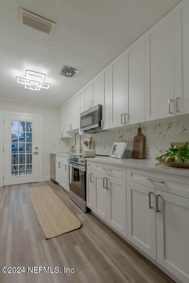 kitchen featuring light wood-type flooring, white cabinetry, stainless steel appliances, and tasteful backsplash