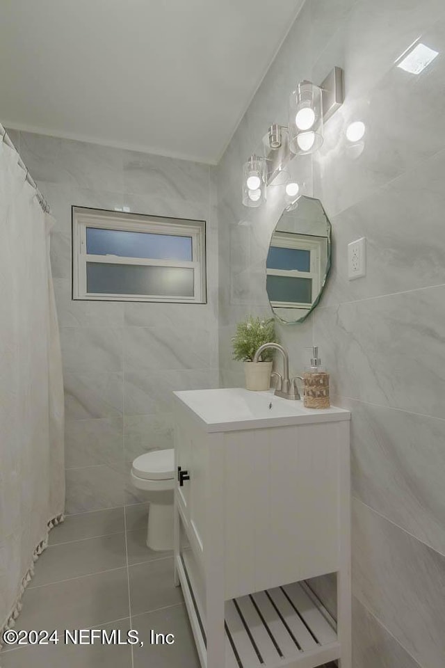 bathroom featuring toilet, vanity, tile patterned floors, and tile walls