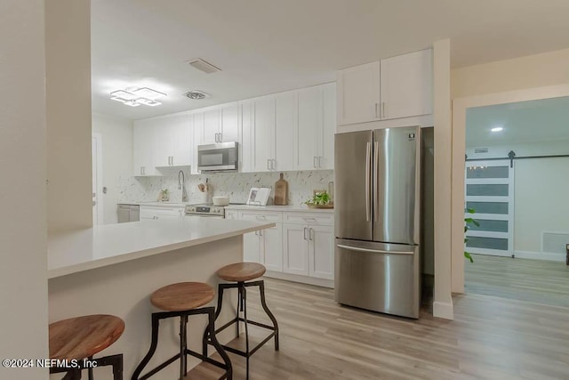 kitchen with a barn door, appliances with stainless steel finishes, light hardwood / wood-style floors, white cabinetry, and a breakfast bar area