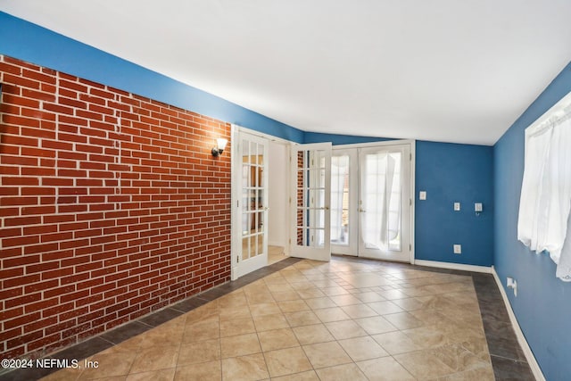 tiled empty room featuring french doors, brick wall, and vaulted ceiling