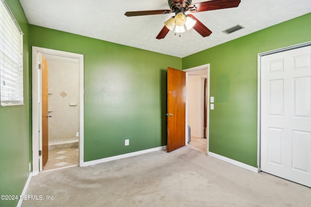 unfurnished bedroom with ceiling fan, a textured ceiling, ensuite bathroom, and light colored carpet