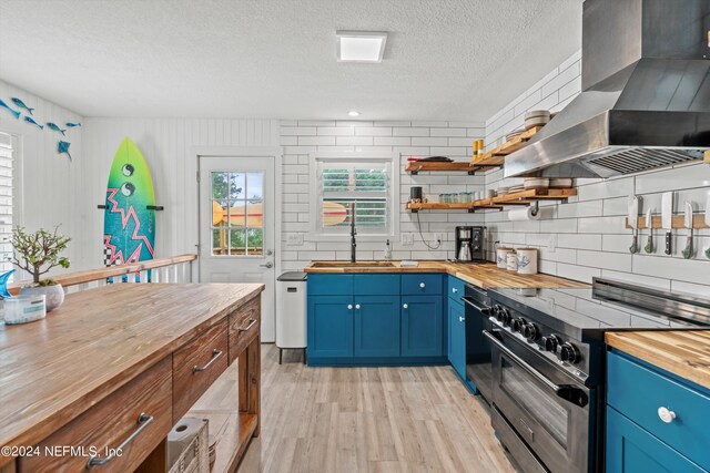 kitchen with wood counters, light wood-type flooring, sink, stainless steel range, and wall chimney exhaust hood