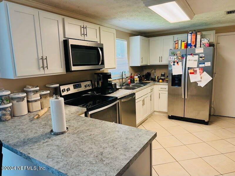 kitchen with white cabinets, sink, a textured ceiling, light tile patterned flooring, and stainless steel appliances