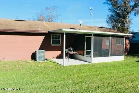 rear view of house featuring a lawn, a sunroom, cooling unit, and a patio