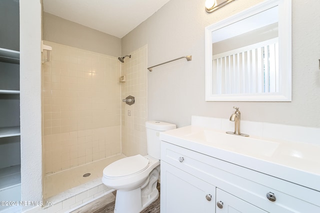 bathroom with toilet, a tile shower, hardwood / wood-style flooring, and vanity