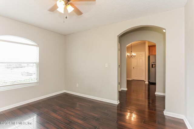 empty room featuring a textured ceiling, ceiling fan with notable chandelier, and dark hardwood / wood-style flooring