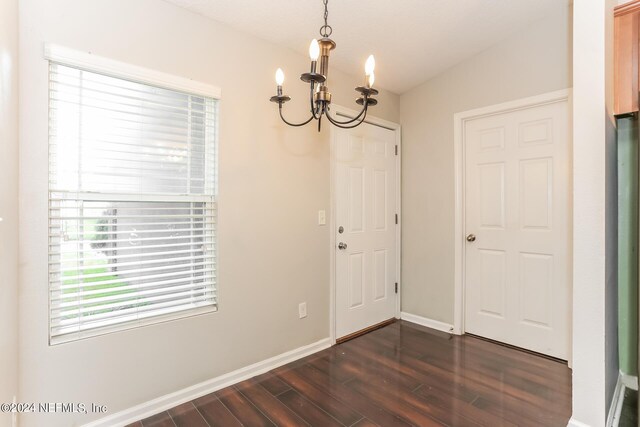 unfurnished dining area featuring an inviting chandelier and dark hardwood / wood-style flooring