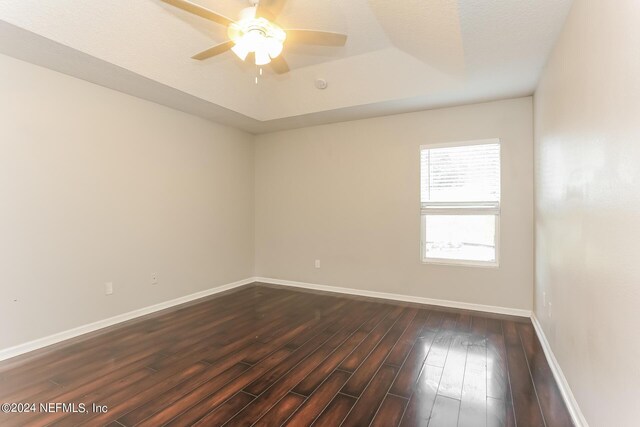 empty room with a tray ceiling, hardwood / wood-style flooring, and ceiling fan