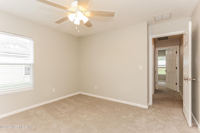 spare room with ceiling fan, plenty of natural light, and light carpet