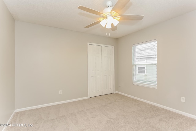 unfurnished bedroom with a textured ceiling, light colored carpet, ceiling fan, and a closet