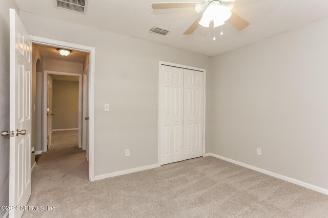 unfurnished bedroom featuring light carpet, ceiling fan, and a closet