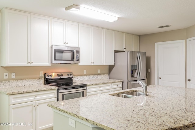 kitchen with light stone countertops, visible vents, a sink, stainless steel appliances, and white cabinetry