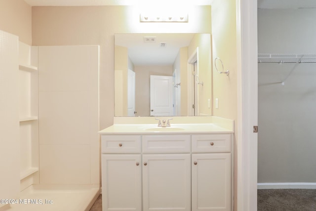 bathroom featuring baseboards, a spacious closet, walk in shower, and vanity