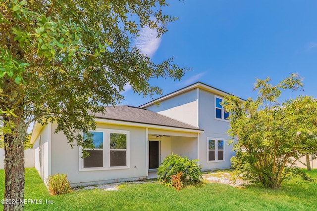 rear view of property with a lawn, ceiling fan, and stucco siding