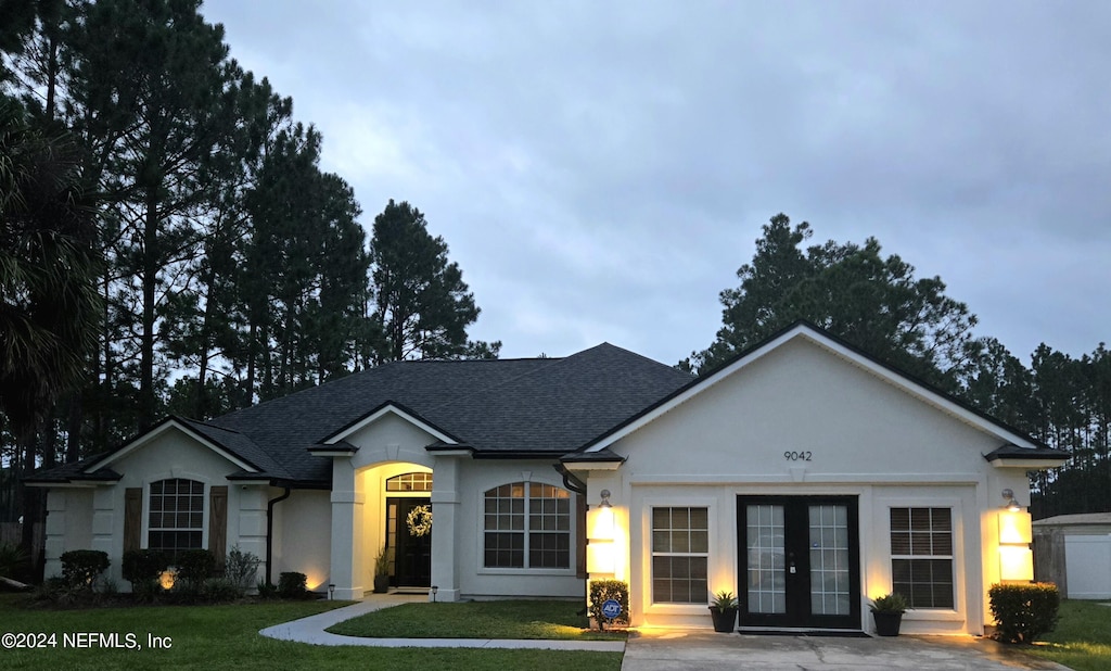 ranch-style home featuring stucco siding, french doors, a front lawn, and roof with shingles