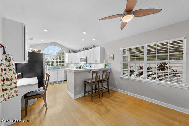 kitchen with vaulted ceiling, light wood-type flooring, white cabinetry, kitchen peninsula, and a breakfast bar area