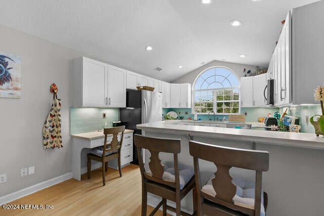 kitchen with white cabinetry, a kitchen bar, decorative backsplash, vaulted ceiling, and light hardwood / wood-style floors