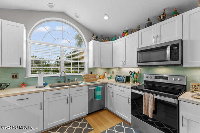 kitchen featuring stainless steel appliances, sink, vaulted ceiling, and white cabinetry