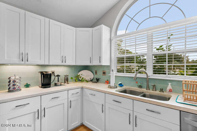 kitchen featuring stainless steel dishwasher, sink, decorative backsplash, and white cabinetry