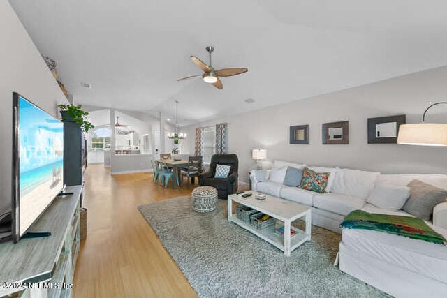 living room with light wood-type flooring, ceiling fan with notable chandelier, and lofted ceiling