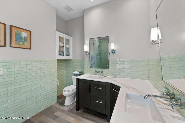 bathroom featuring toilet, a shower, tile walls, wood-type flooring, and vanity