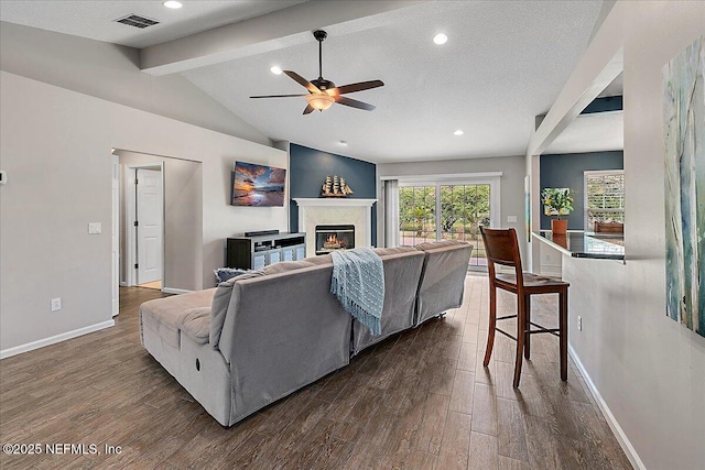 living room featuring dark hardwood / wood-style flooring, a textured ceiling, ceiling fan, and vaulted ceiling with beams