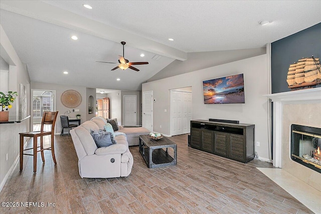 living room with lofted ceiling with beams, a fireplace, ceiling fan, and a textured ceiling