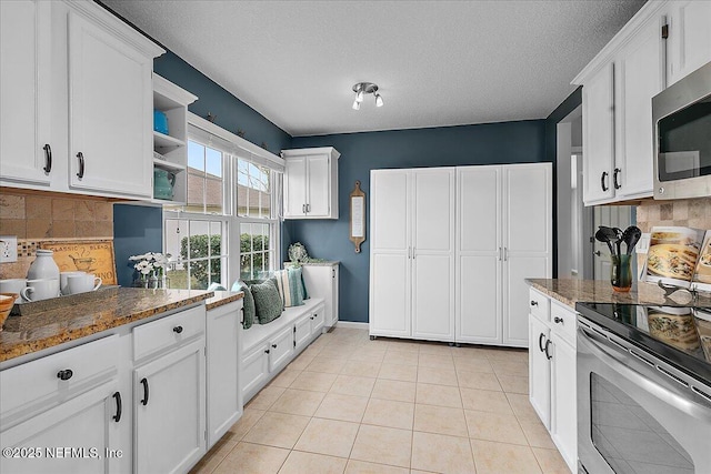 kitchen featuring appliances with stainless steel finishes, dark stone counters, a textured ceiling, white cabinetry, and backsplash