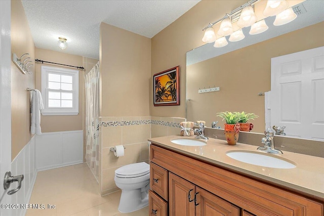 bathroom featuring a textured ceiling, tile walls, toilet, tile patterned floors, and vanity