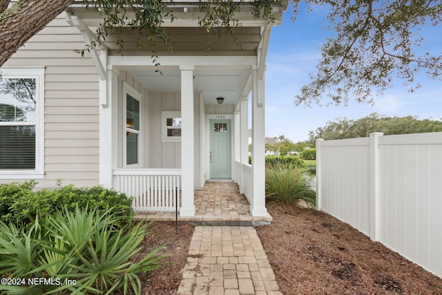 doorway to property featuring covered porch and fence