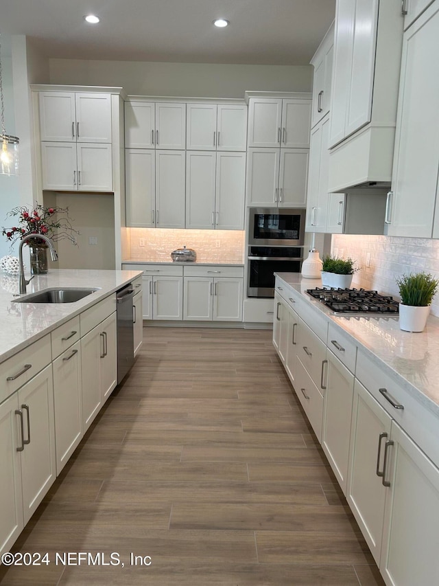 kitchen with light wood-type flooring, stainless steel appliances, light stone counters, and sink