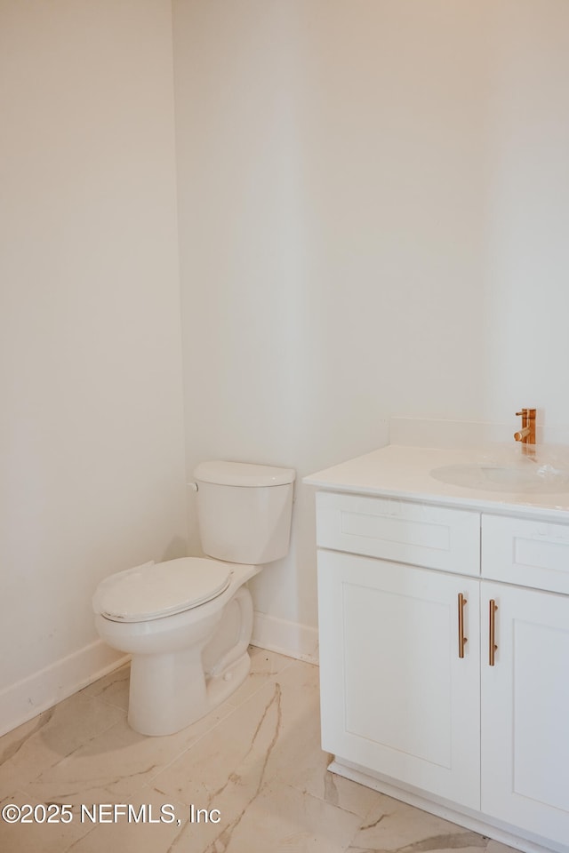 bathroom with marble finish floor, vanity, toilet, and baseboards