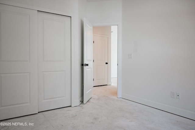 unfurnished bedroom featuring concrete floors, a closet, and baseboards