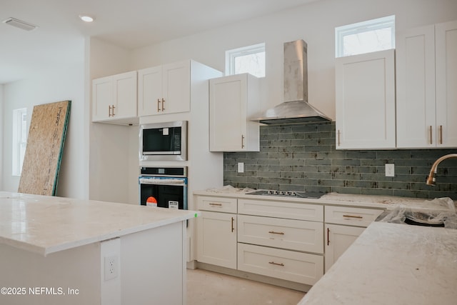 kitchen featuring light stone counters, decorative backsplash, built in microwave, oven, and wall chimney exhaust hood