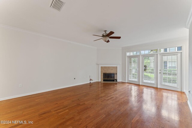 unfurnished living room featuring ceiling fan, ornamental molding, a tile fireplace, and hardwood / wood-style flooring