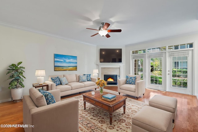 living room featuring light wood-style floors, a lit fireplace, a ceiling fan, and crown molding