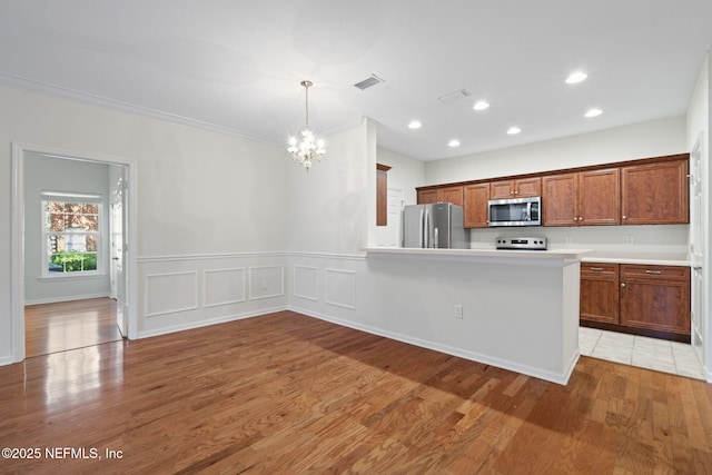kitchen with light wood-style floors, an inviting chandelier, brown cabinetry, visible vents, and appliances with stainless steel finishes