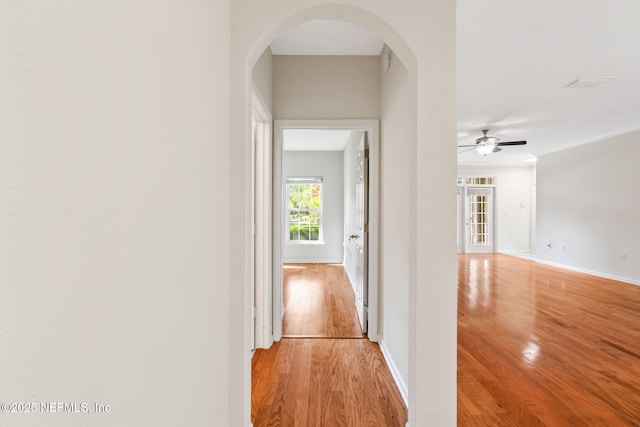 corridor featuring arched walkways, light wood-type flooring, and baseboards